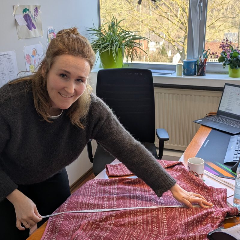 Ramona misst die Rueckenlaenge eines Oberteils vom Kragenansatz bis zum Saum