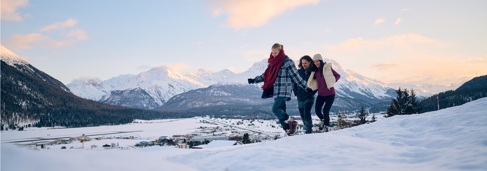 Gruppe in warmer Winterbekleidung beim Spaziergang im Schnee vor Bergpanorama